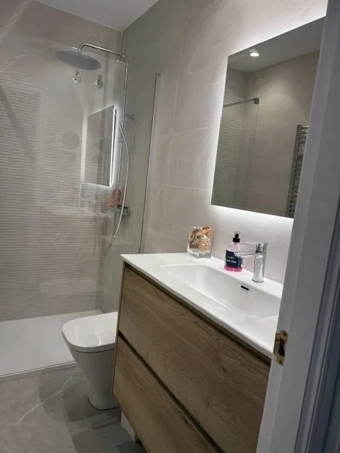 Baño con lavabo sobre mueble de madera y espejo con luz