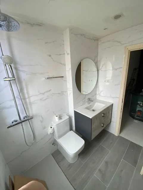 Baño con mueble azul, espejo redondo y ducha