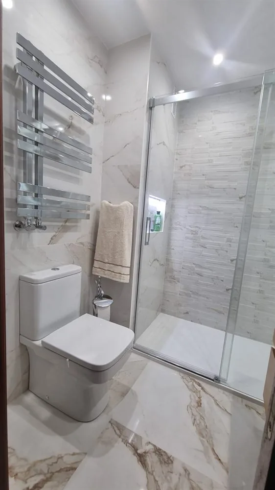 Baño con mampara de cristal y radiador toallero