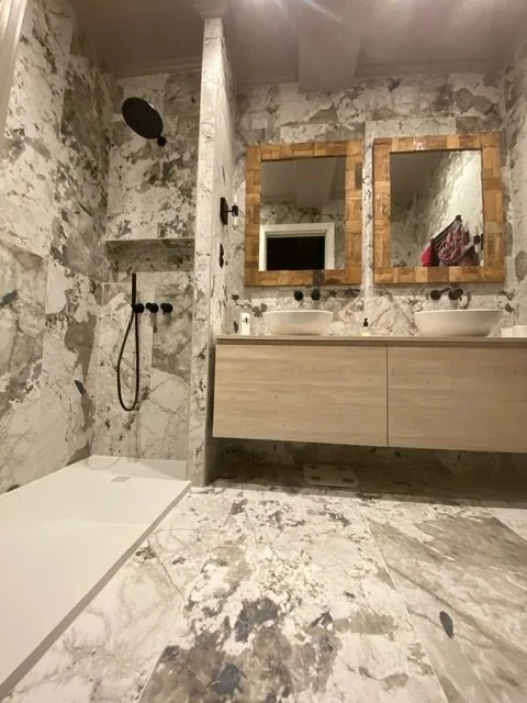 Baño de mármol con doble lavabo y espejos con marco de madera