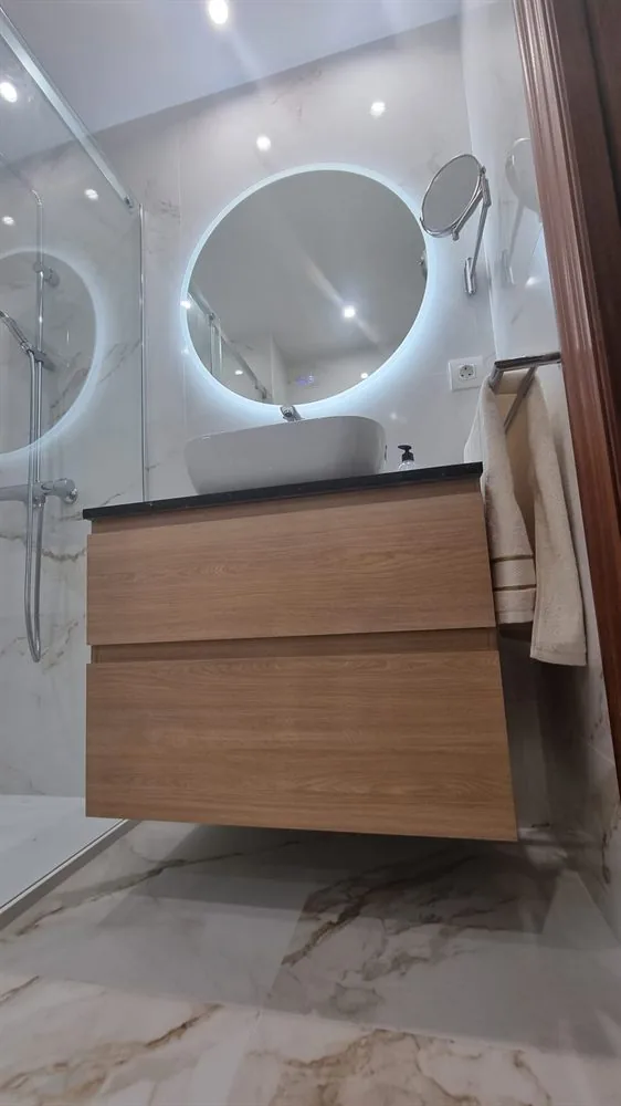 Baño con mueble de madera y espejo redondo retroiluminado