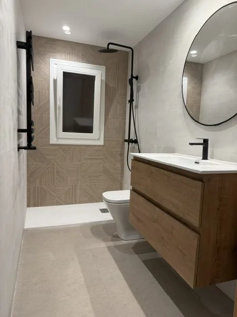 Baño con ducha, espejo redondo y mueble suspendido de madera