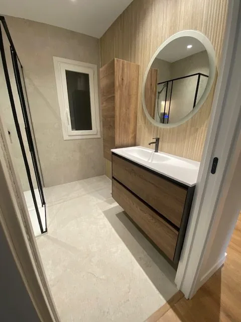 Baño con mueble de madera, espejo redondo y ventana