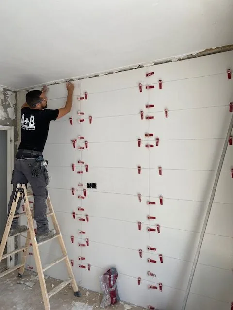 Operario de A+B alicatando una pared subido a una escalera